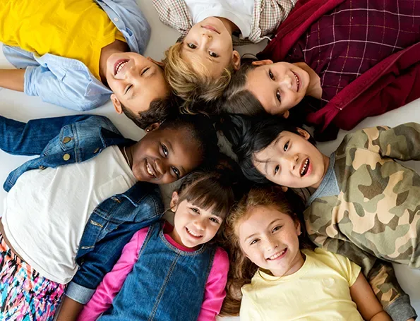 Smiling children lying in a circle with their heads together
