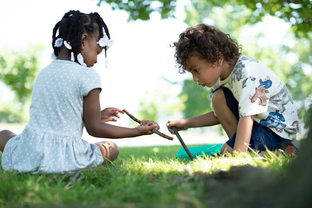 Two children playing with a stick in the grass