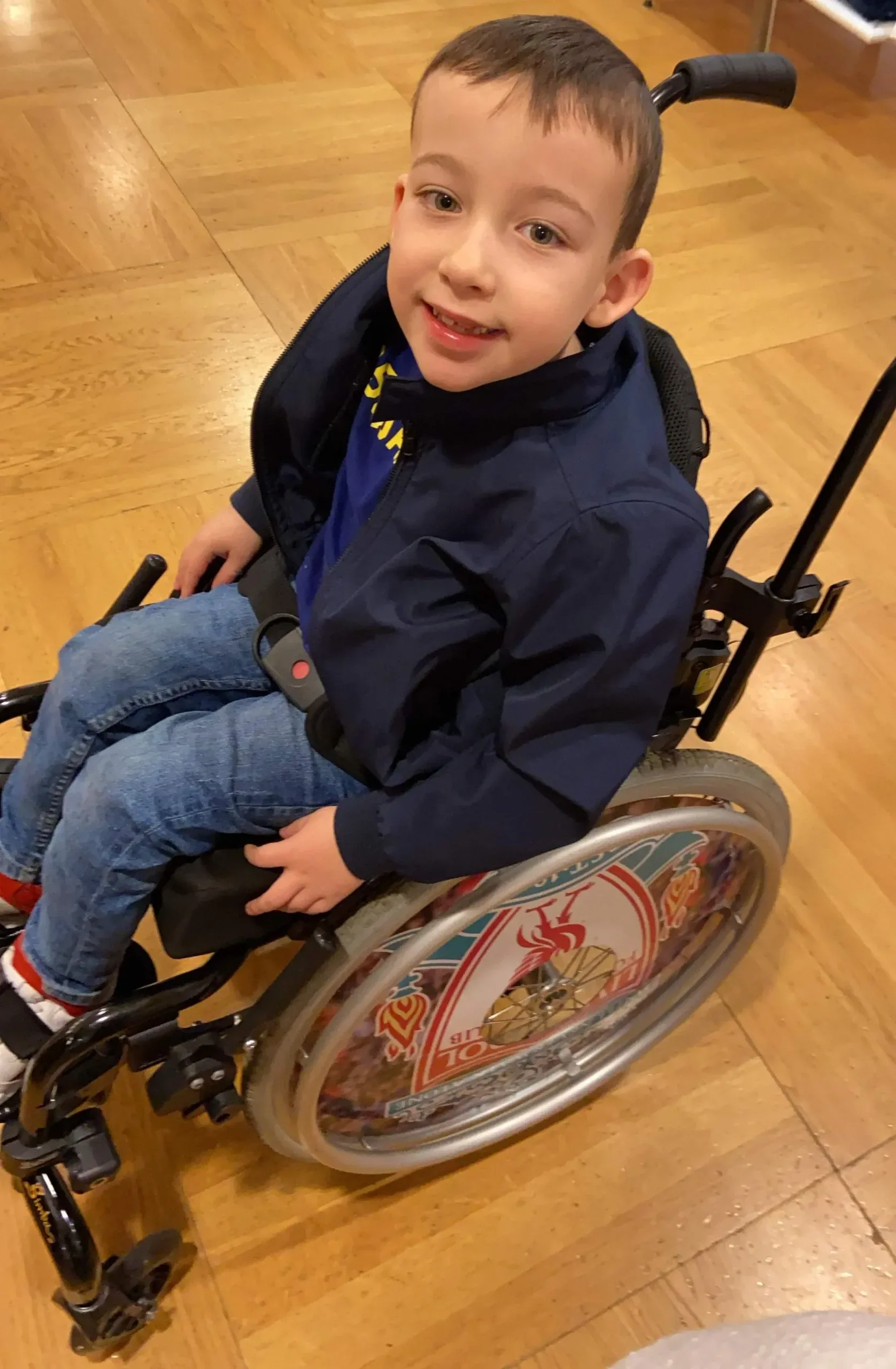 Smiling young boy sitting in a pediatric wheelchair at home