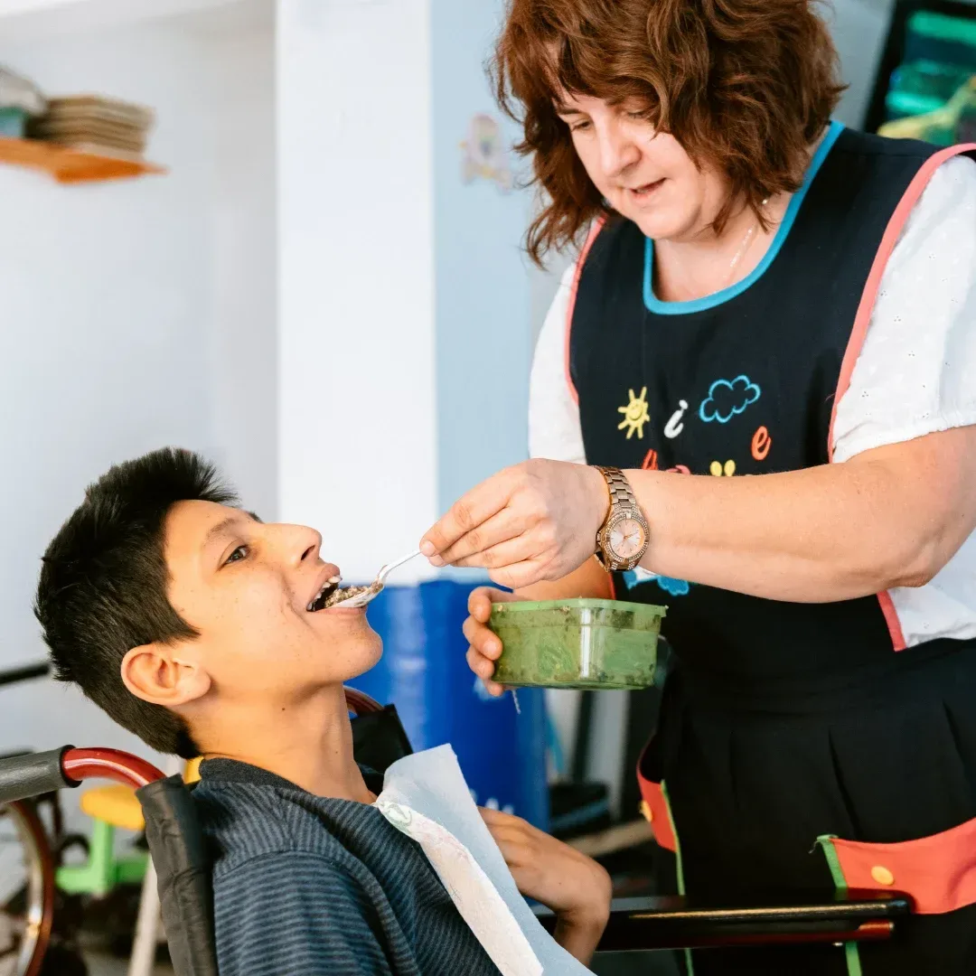 Caregiver helping a boy in a wheelchair eat a meal