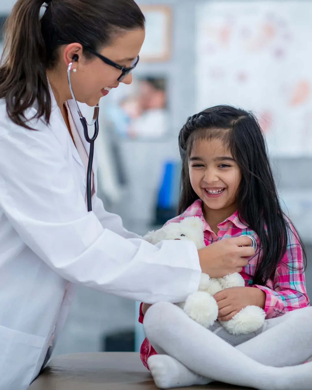 Doctor listening to a smiling girl's heartbeat with a stethoscope