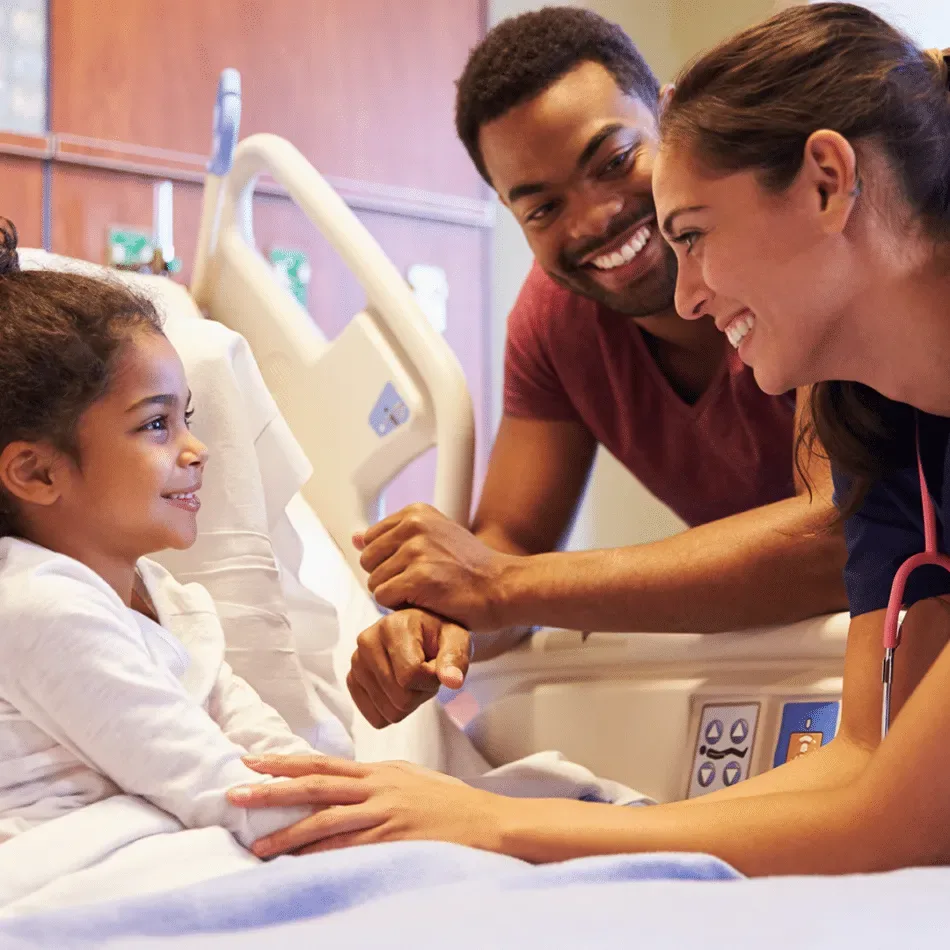 Nurse and father comforting a smiling girl in a hospital bed