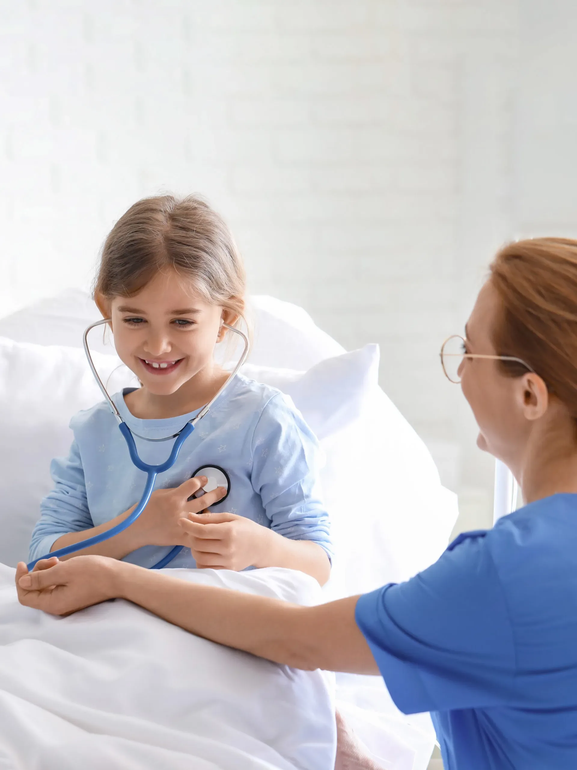 Nurse checking a smiling girl in bed with a stethoscope
