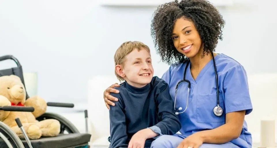 Nurse smiling with a boy sitting beside his wheelchair