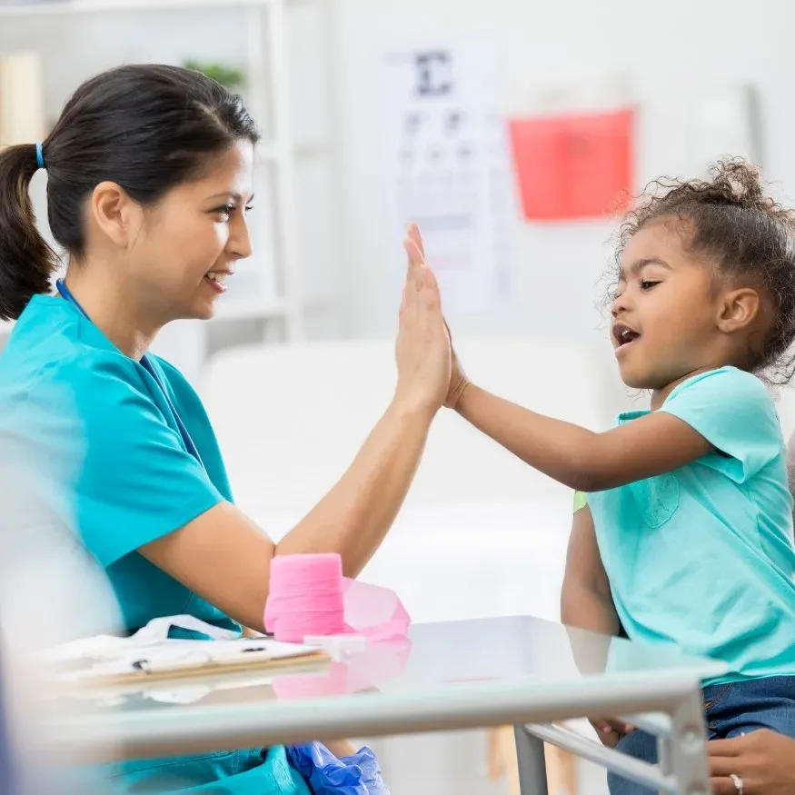 Pediatric nurse giving a young girl a high five during a checkup