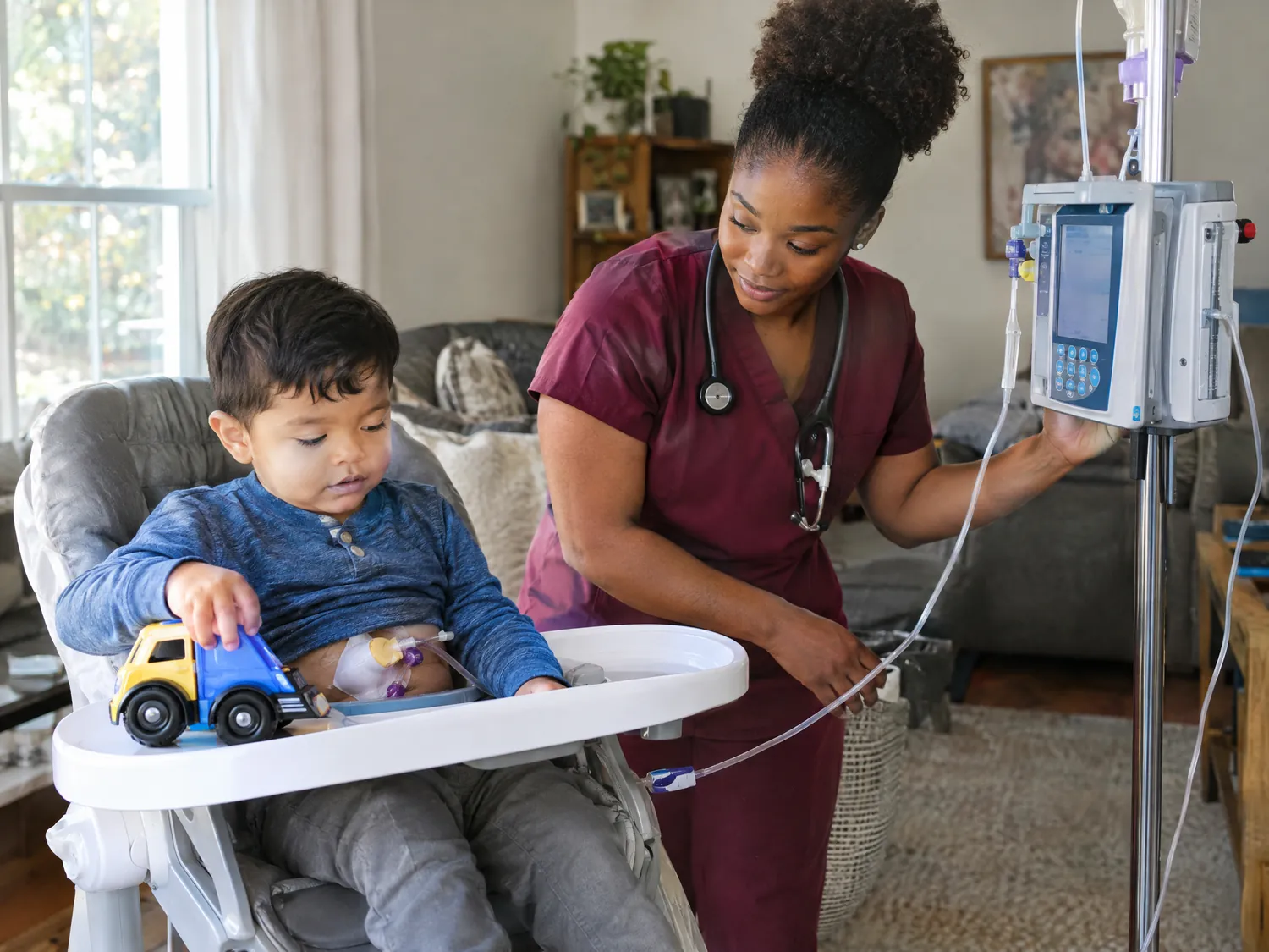 Nurse checking a feeding pump for a toddler boy in a high chair