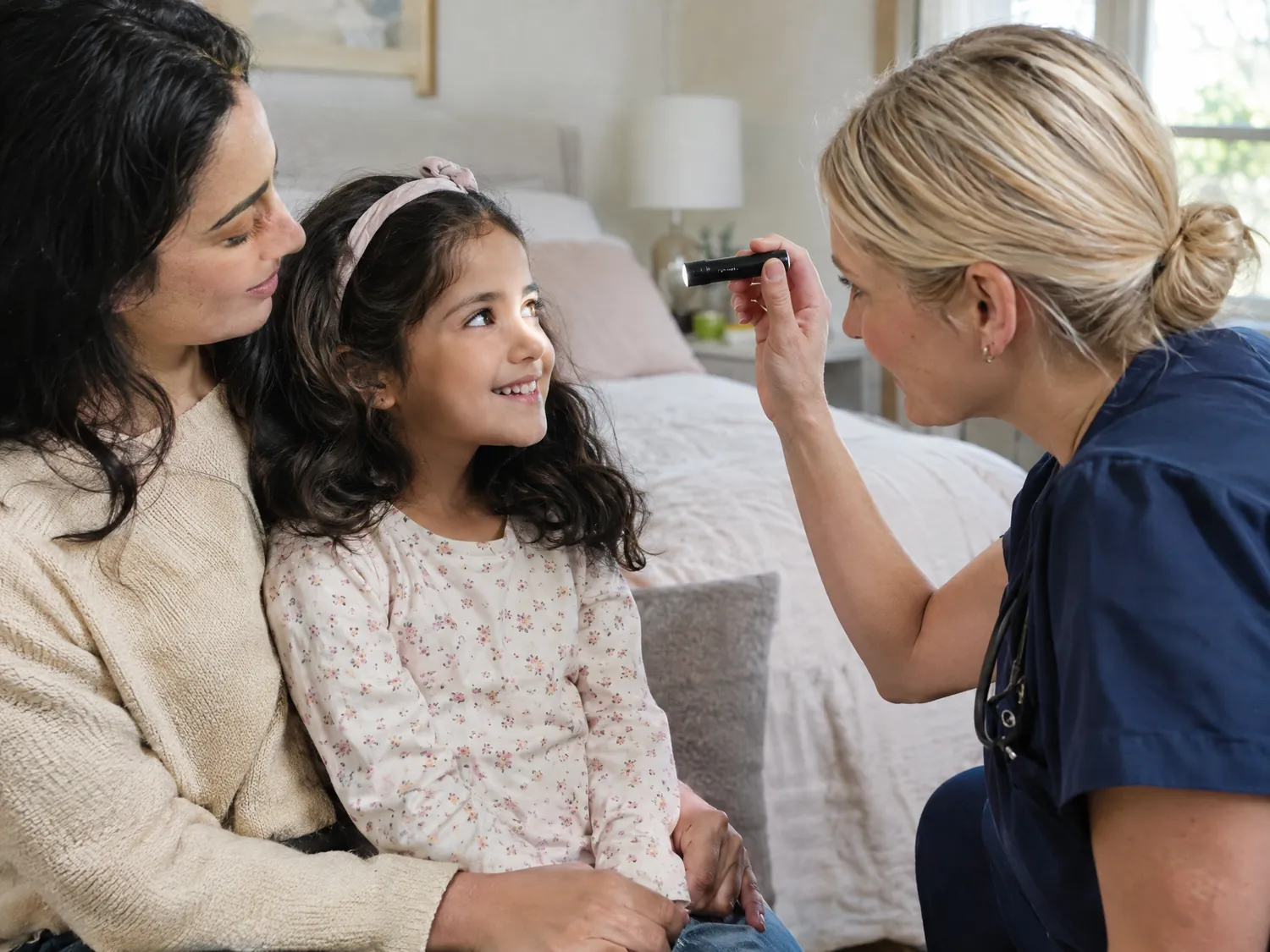 Nurse gently checking a girl’s eyes as she sits on her mother’s lap
