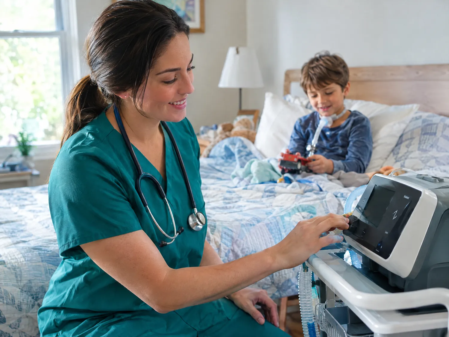 Nurse checking a home ventilator beside a boy in bed